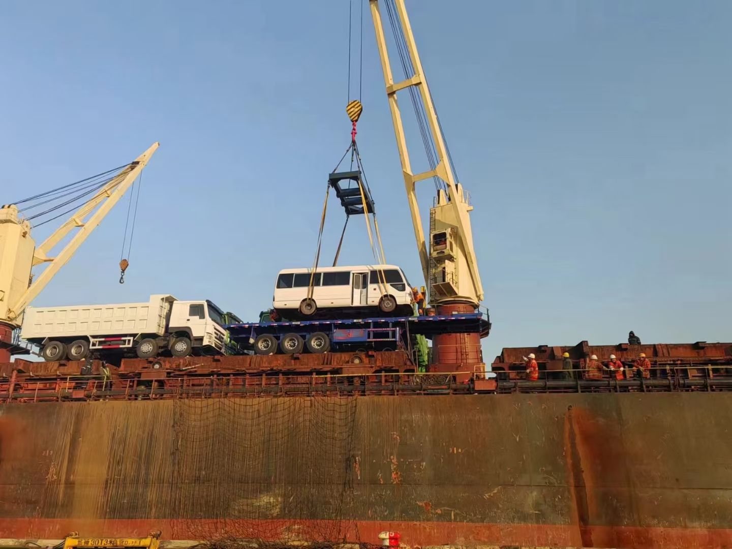 Dump trucks and a coach stowed side by side on the deck of a breakbulk vessel during loading