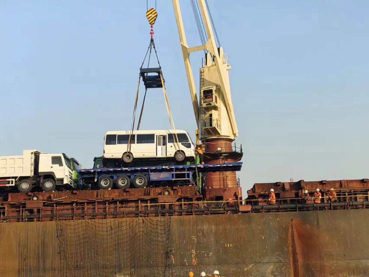 A bus lowered towards the vessel deck by ship's crane, slung with webbing straps