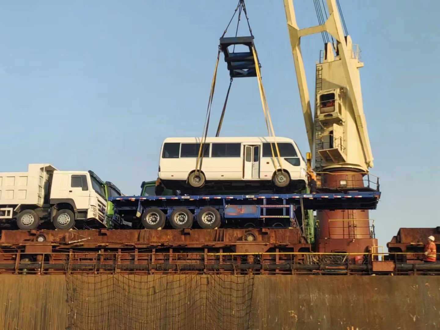 A coach lifted by a vessel's crane on a spreader frame during breakbulk loading at a Chinese port