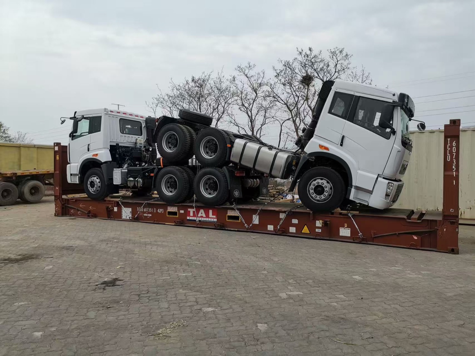 Two tractor heads stacked offset on a flat rack, side view