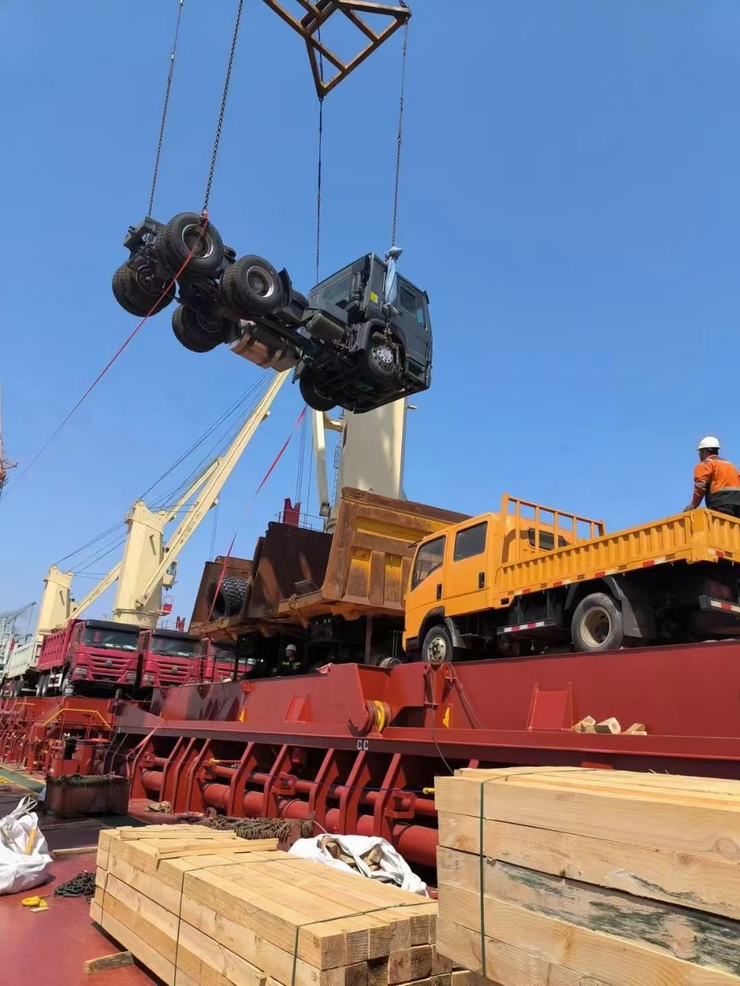 A truck tractor head lifted by a harbour crane on a wooden spreader frame
